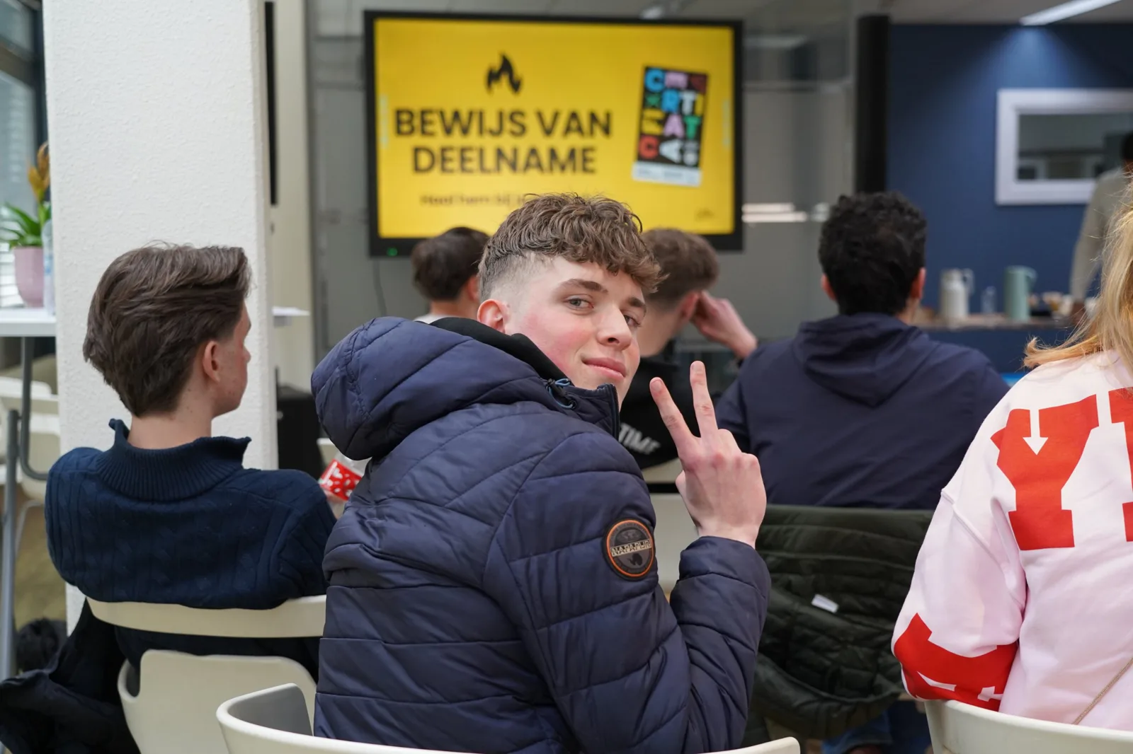 Student kijkt lachend om en maakt een peace-teken tijdens een training