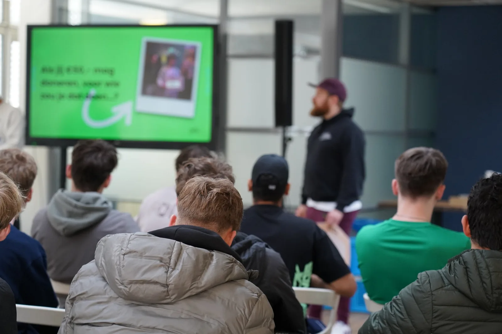 Trainer van Ollie voor een groep studenten, op het scherm een vraag voor de klas
