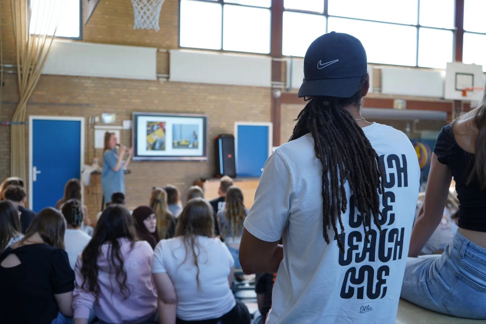 Chudi Uzozie in een Each one teach one-shirt kijkt naar een training in een gymzaal